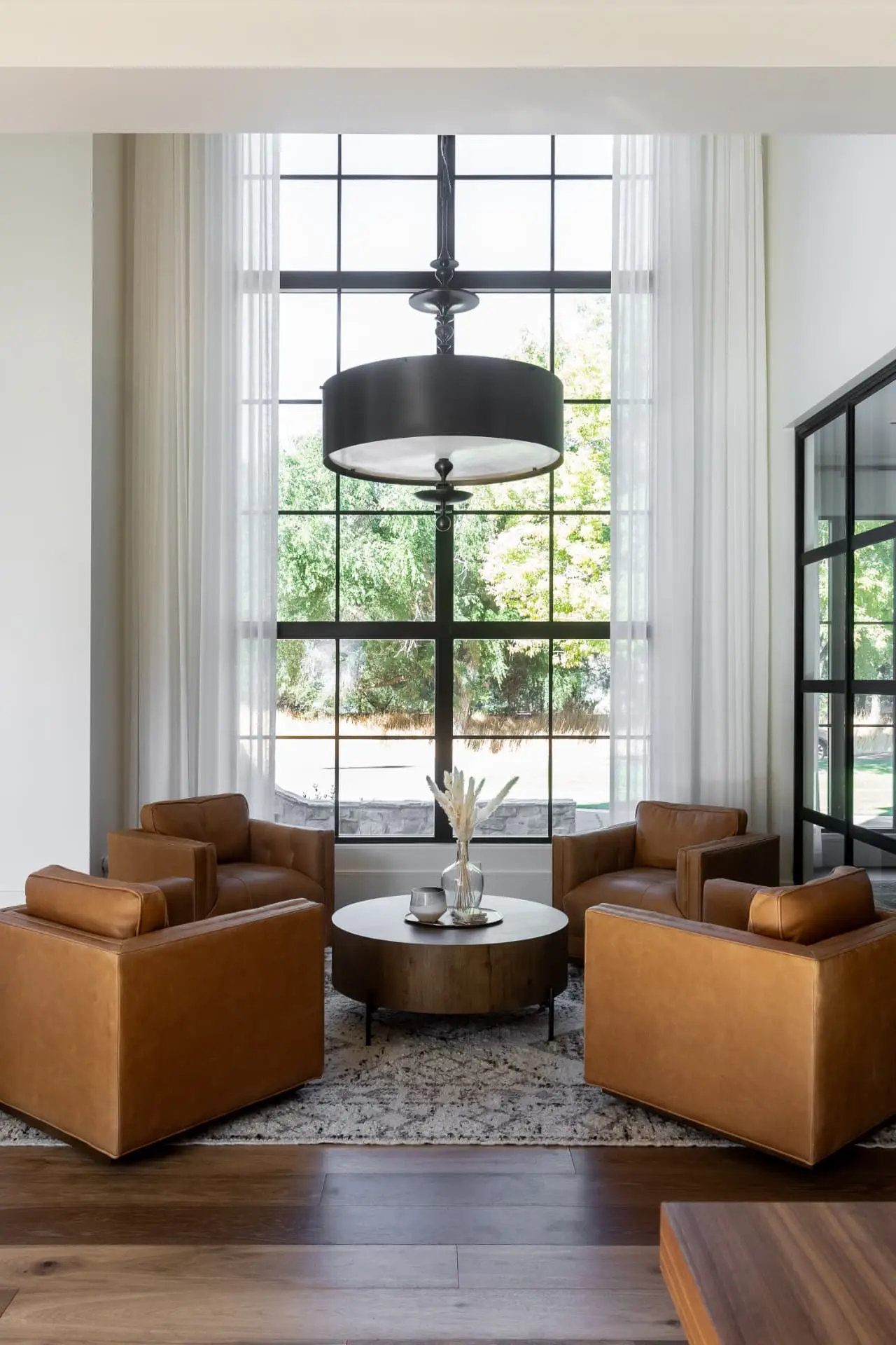 Dark drum pendant with an alabaster diffuser above four leather chairs at a tall window
