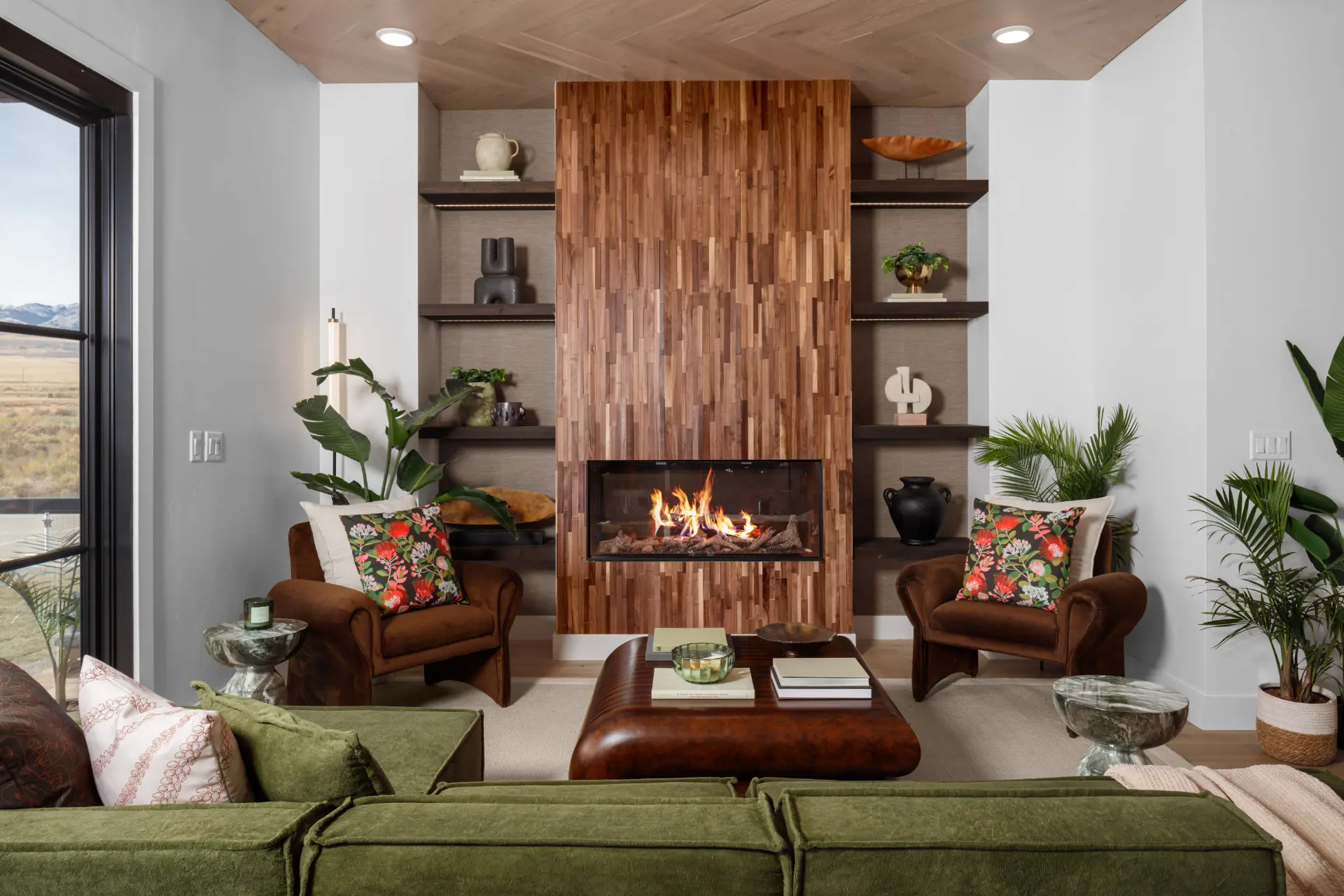 Fireplace wall in mixed wood tile flanked by lit floating shelves and velvet chairs