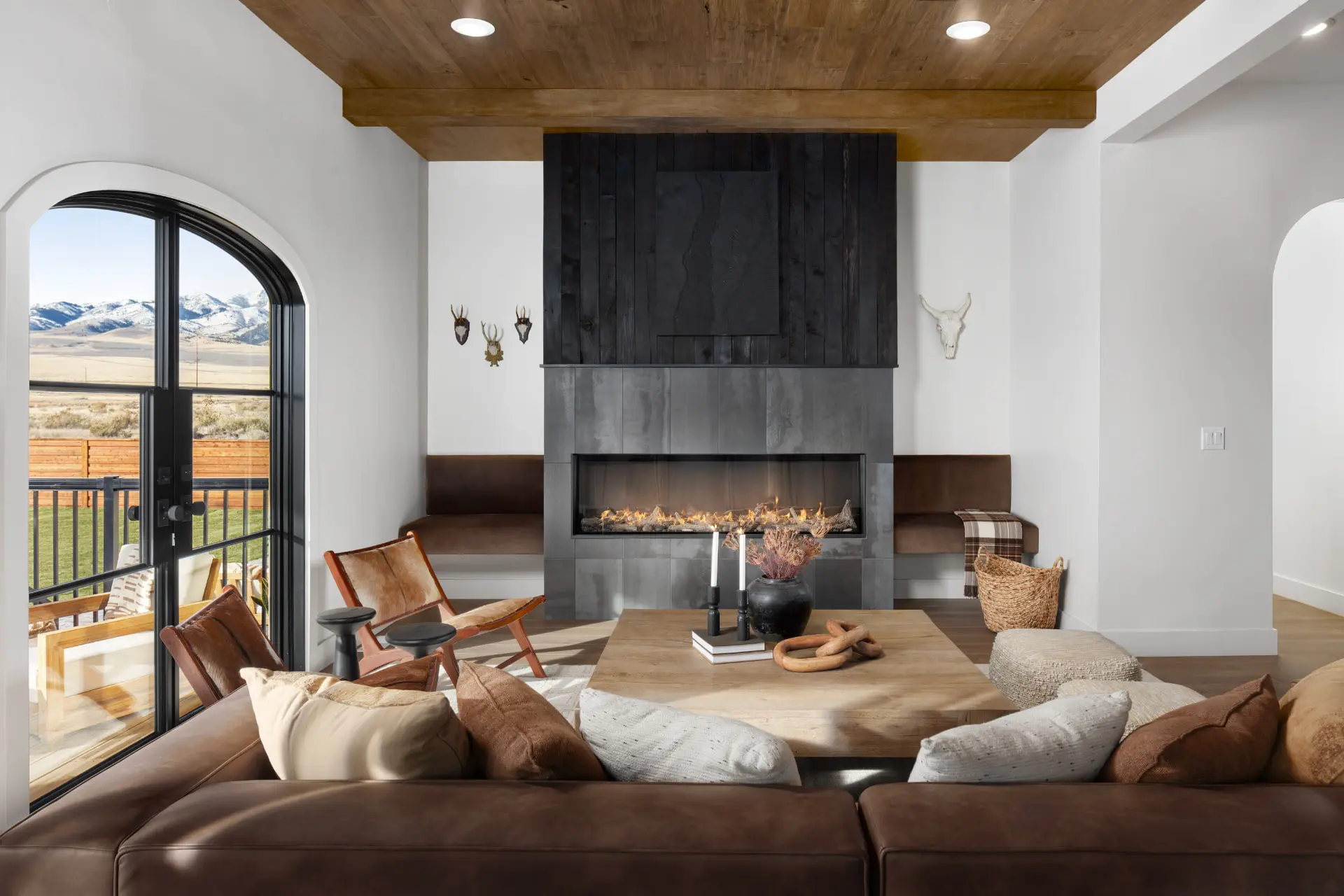 Living room with a blackened steel linear fireplace, leather sectional and arched steel door to the deck