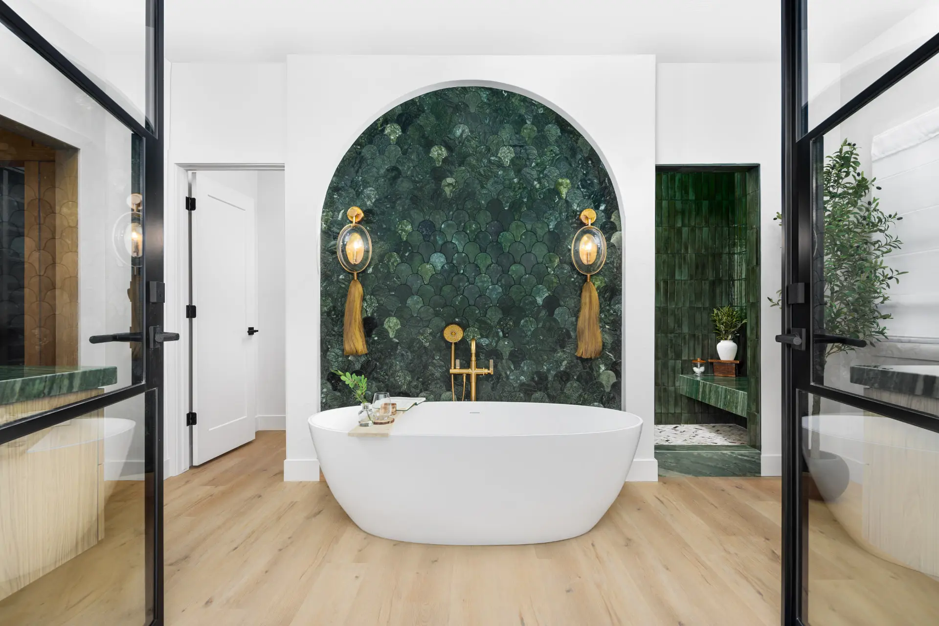 Freestanding tub in an arched green tile alcove framed by globe tassel sconces