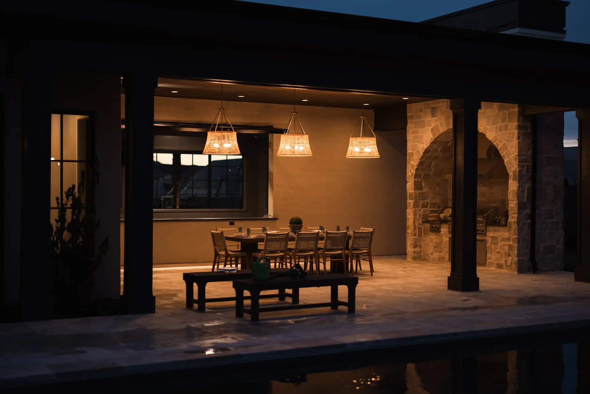 Covered patio dining lit by three woven pendants at dusk