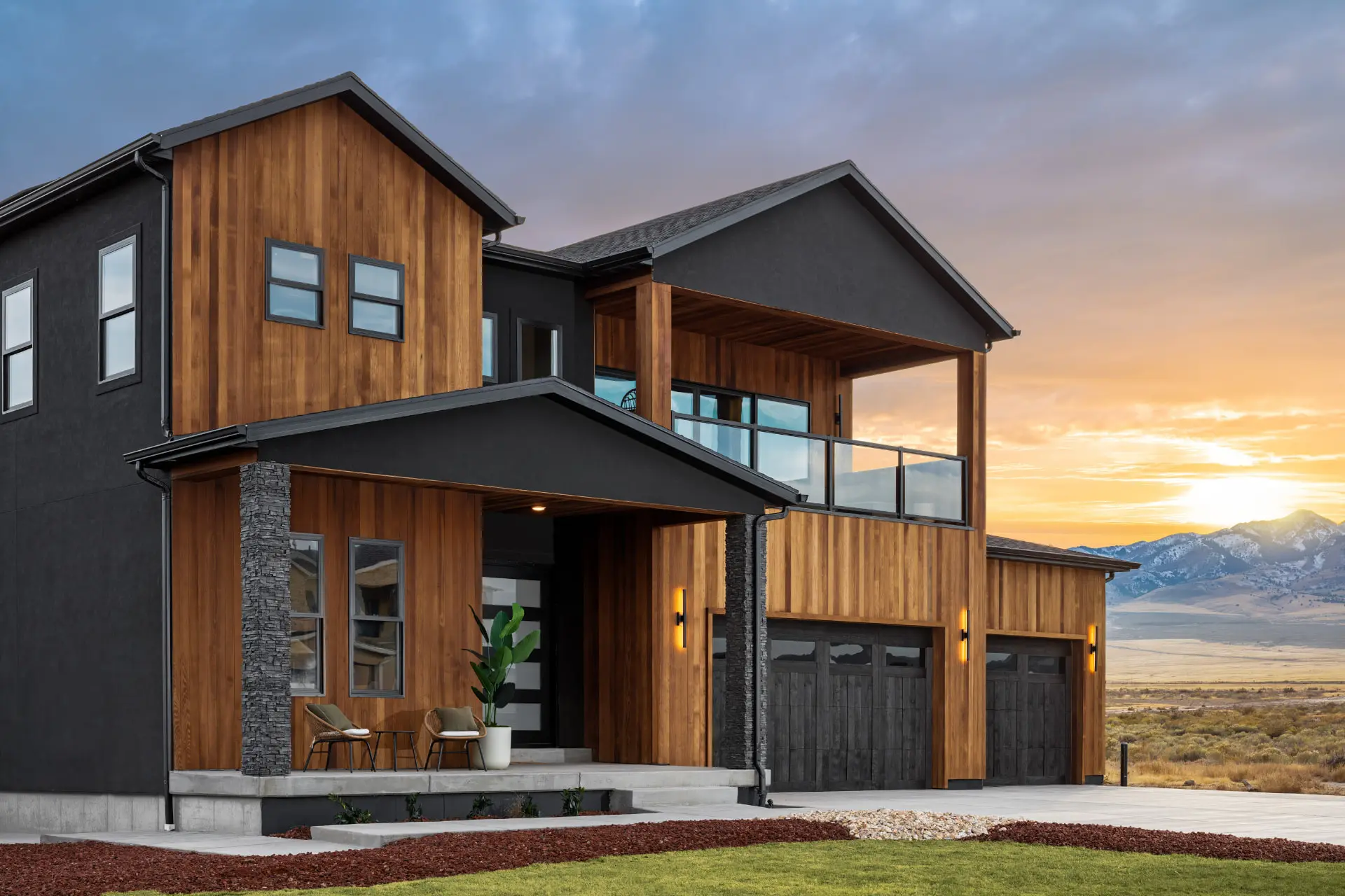 Cedar and black stucco exterior at sunset with amber linear sconces at the entry and garage