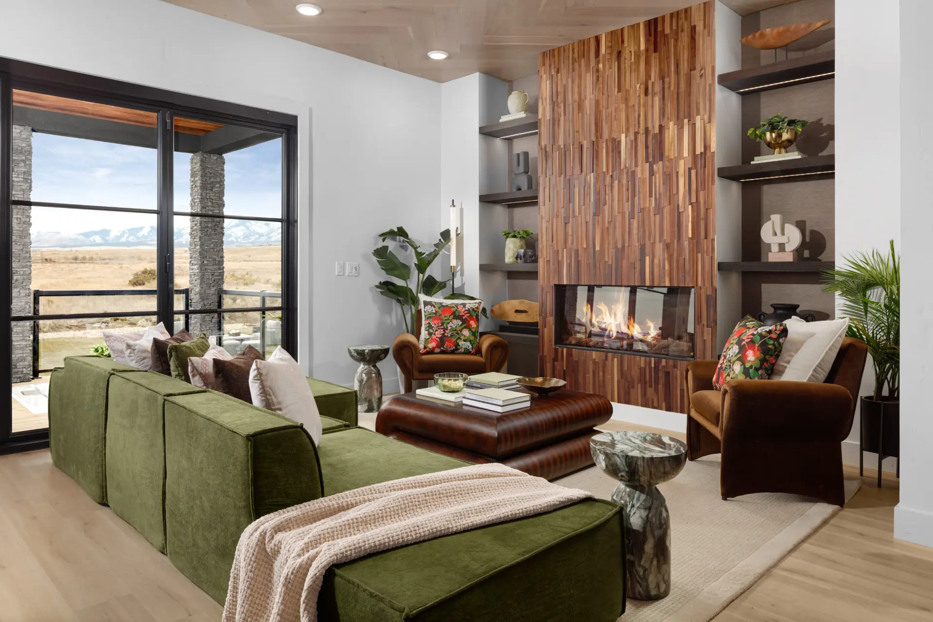 Great room with a stacked wood fireplace, green sectional and valley views through steel doors