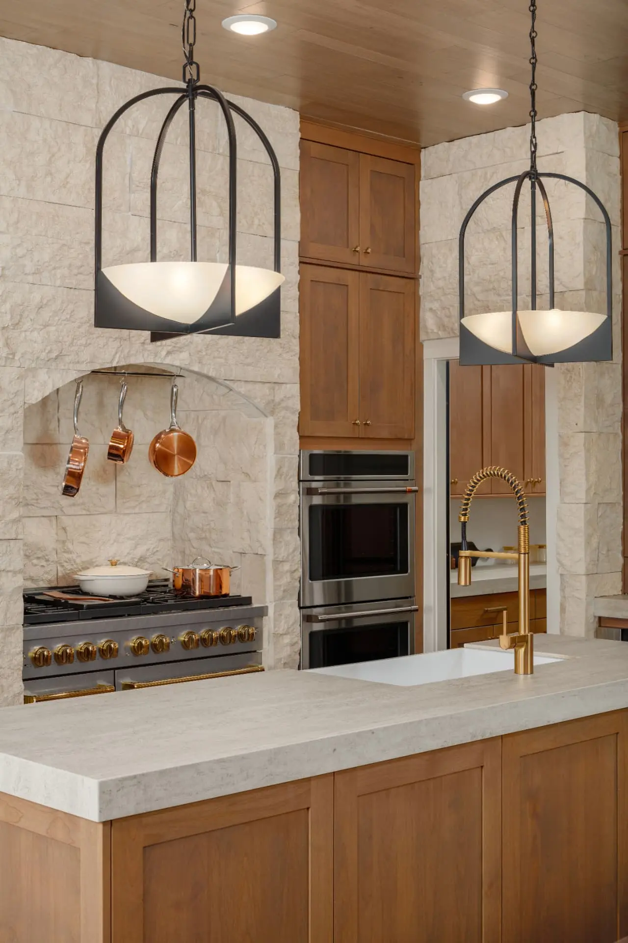 Kitchen island detail with two arched iron pendants and alabaster bowl shades over stone
