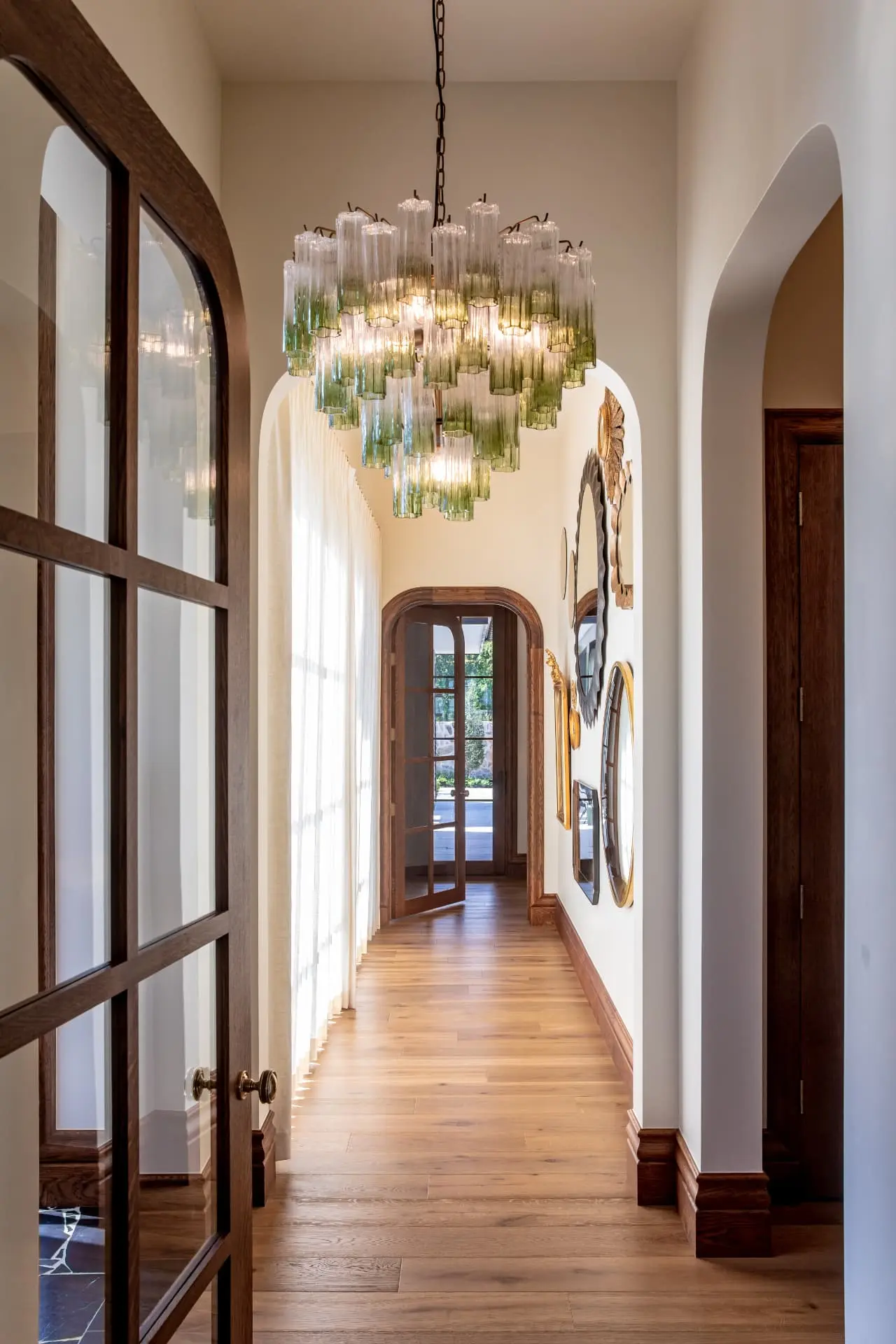 Green and clear glass tube chandelier in an arched gallery hallway
