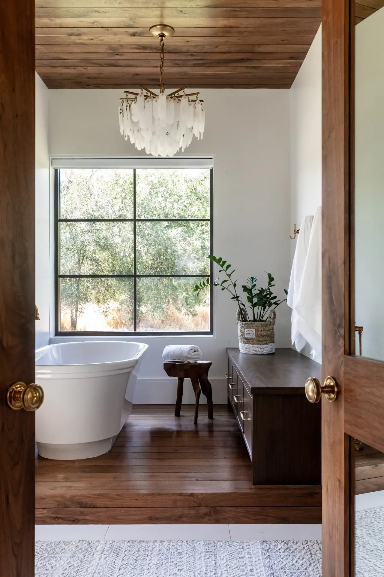 Frosted glass tiered chandelier over a freestanding tub beneath a wood-plank ceiling