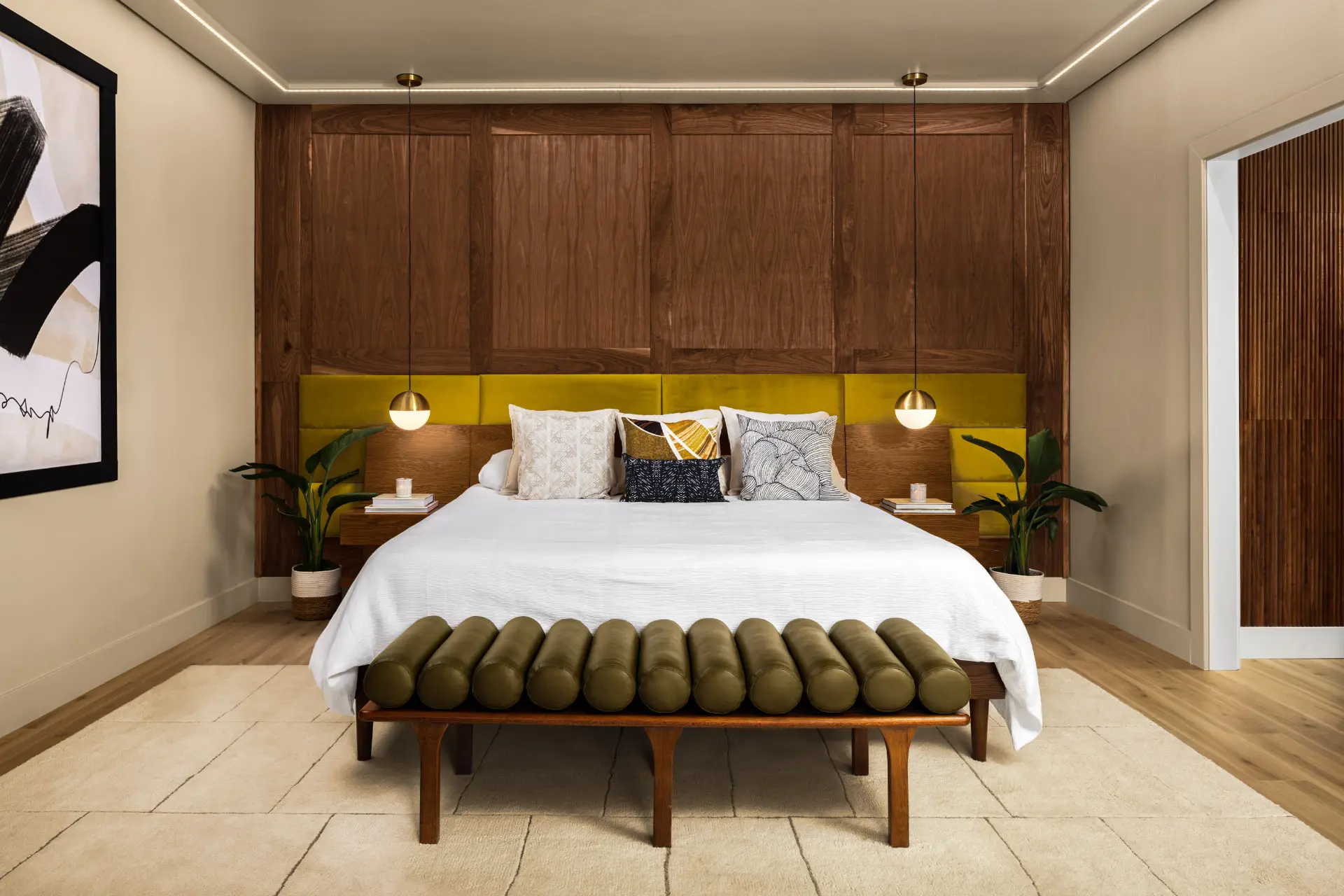 Primary bedroom with a walnut panel wall, chartreuse headboard and brass globe pendants