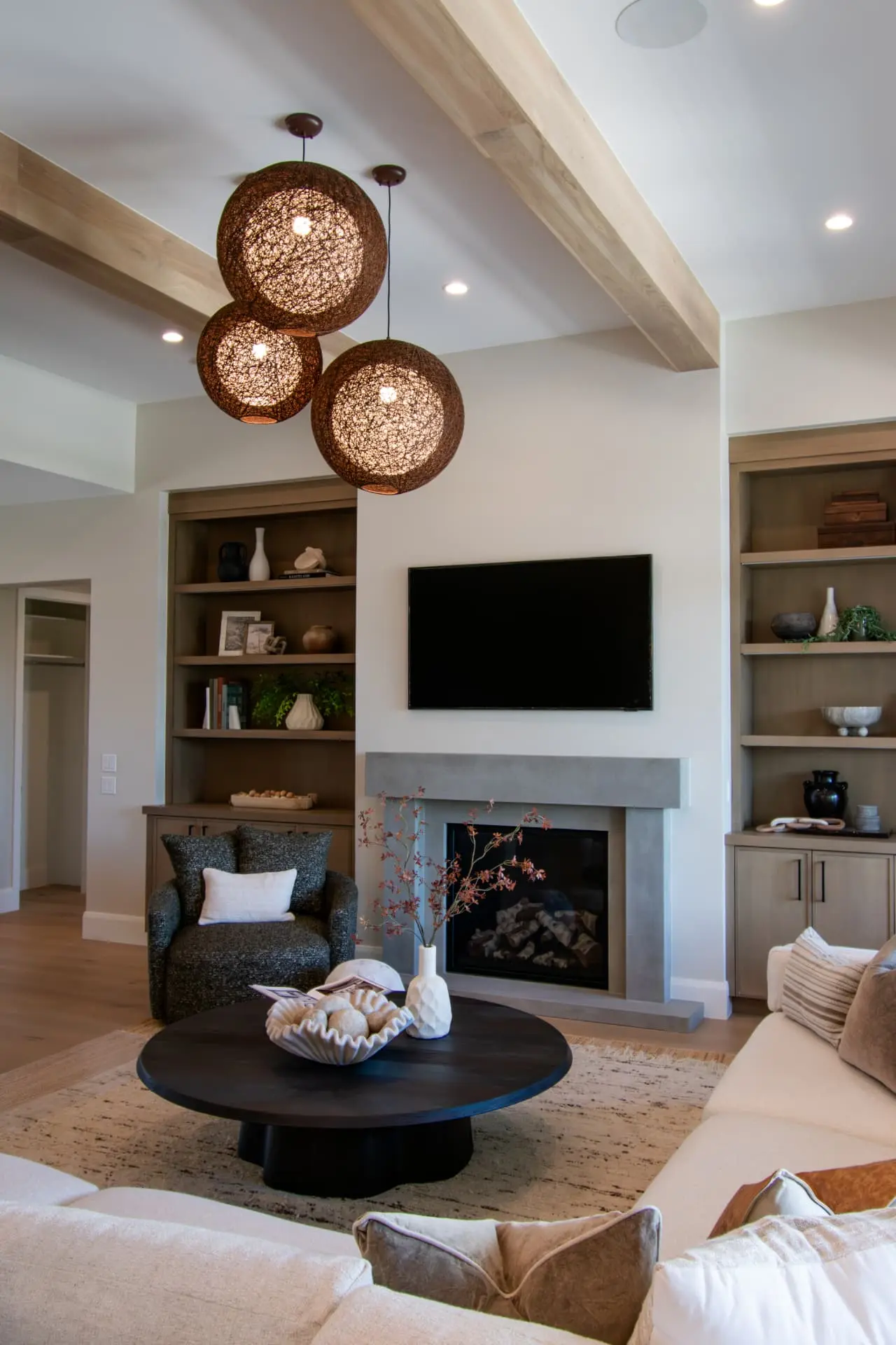 Living room with beamed ceiling, concrete fireplace surround and three woven globe pendants