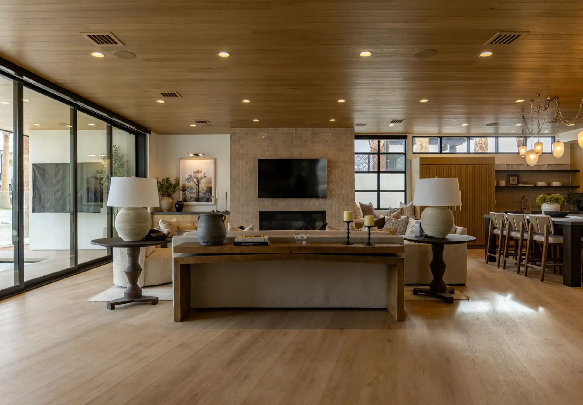 Open living and kitchen under a wood-clad ceiling with glass pendants