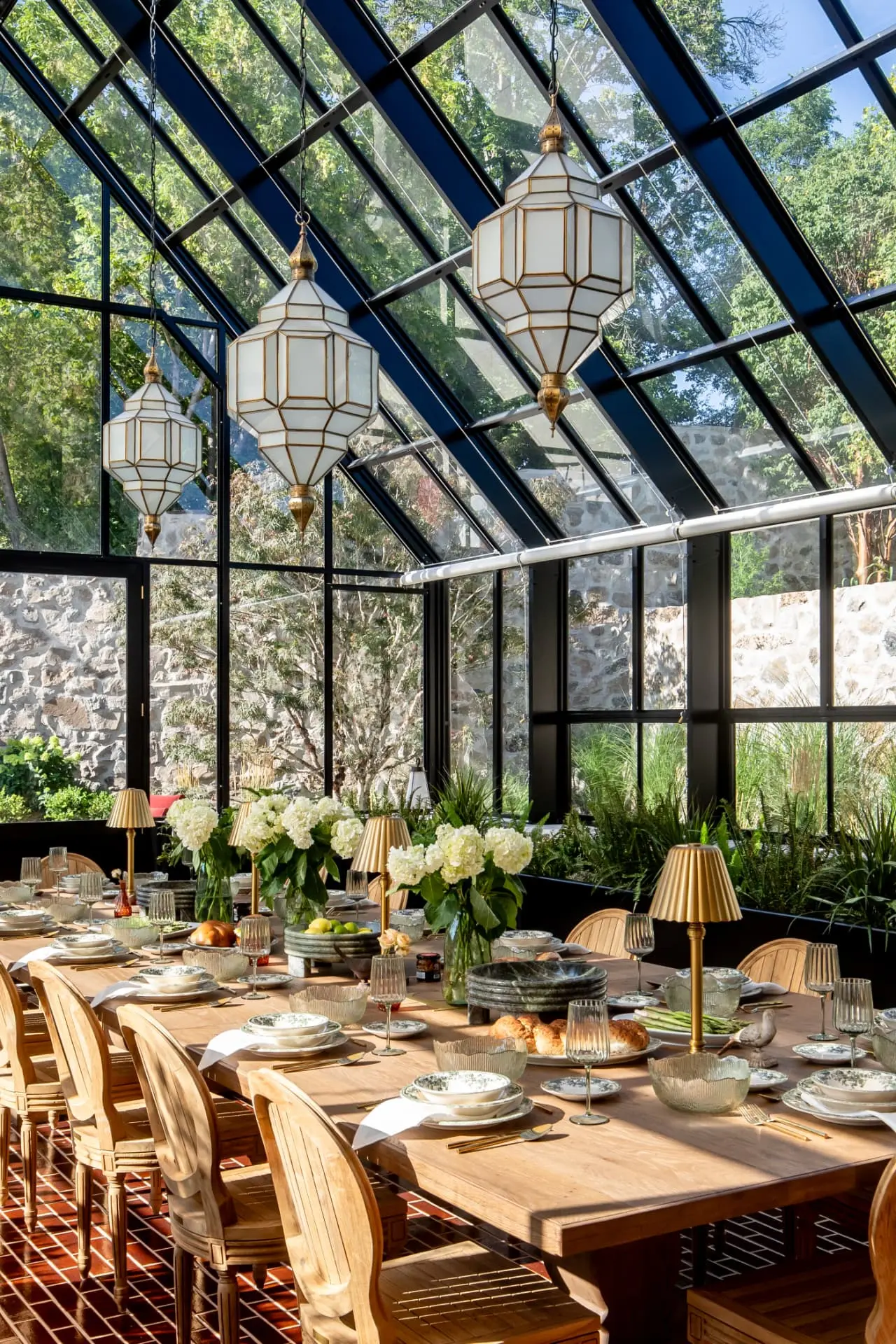 Three antique brass lanterns hung in a glass conservatory over a long banquet table
