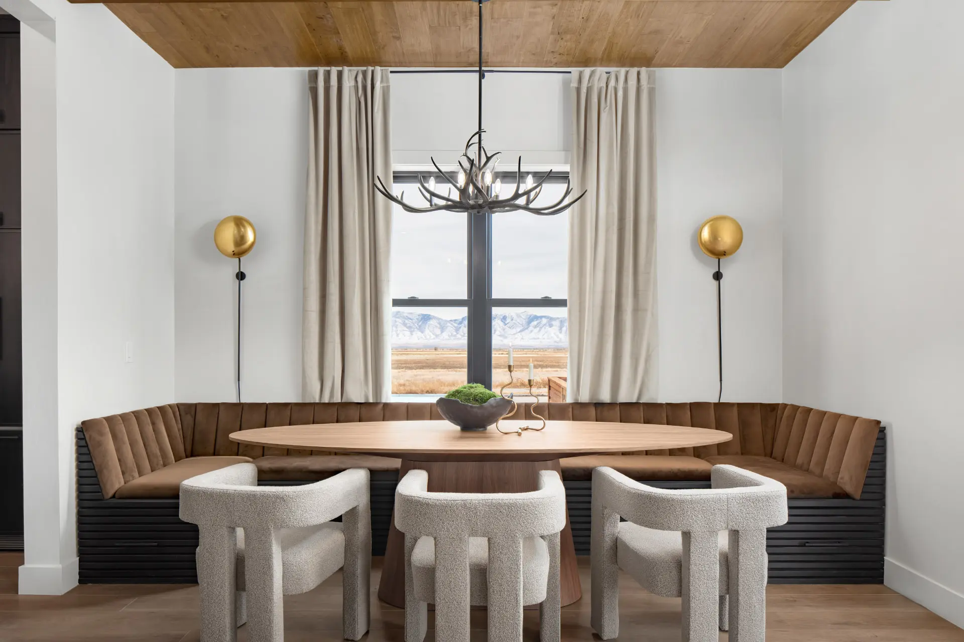 Oval dining table with a curved banquette, antler chandelier and brass dome sconces