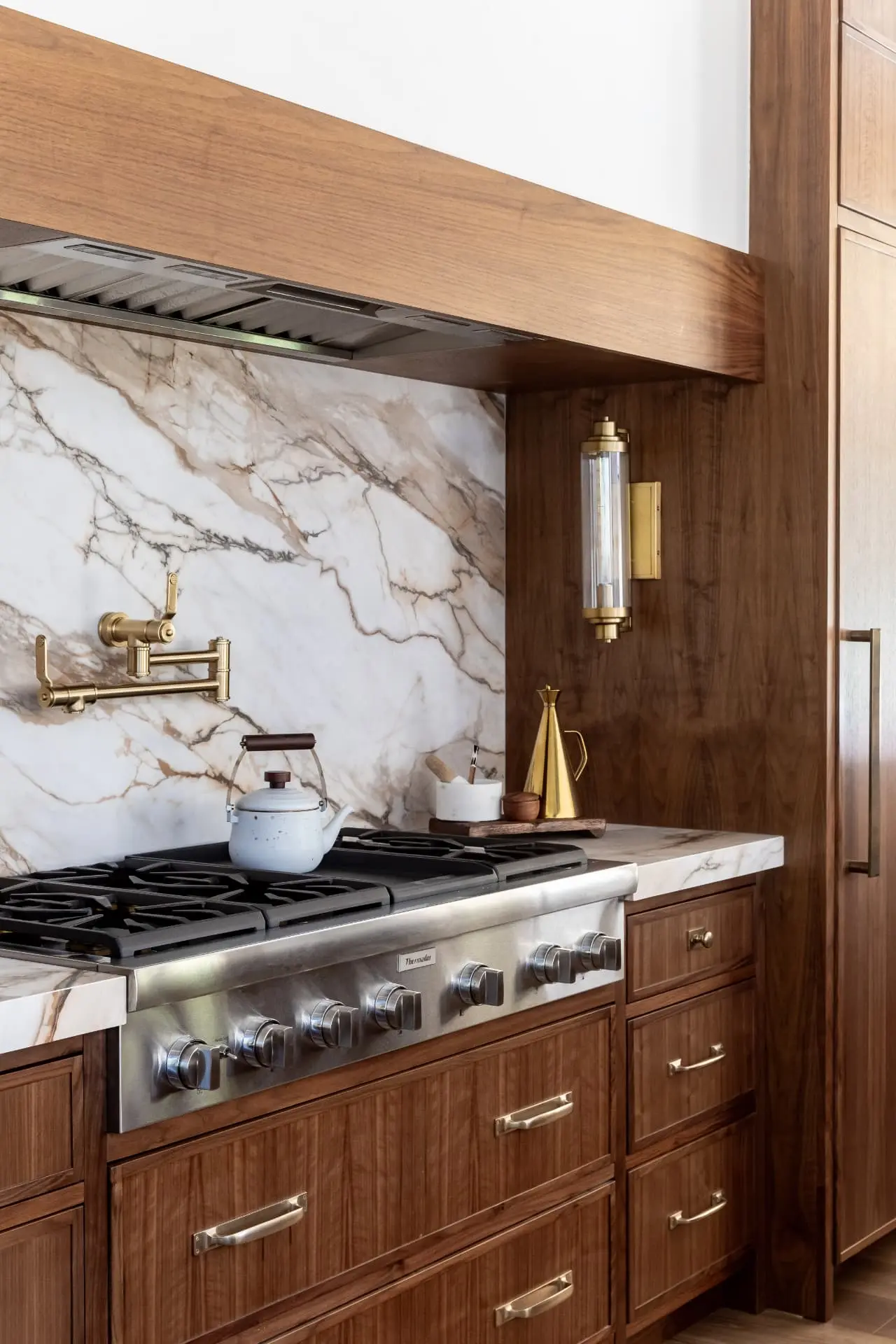 Brass and glass tube sconce beside a marble range wall in a walnut kitchen