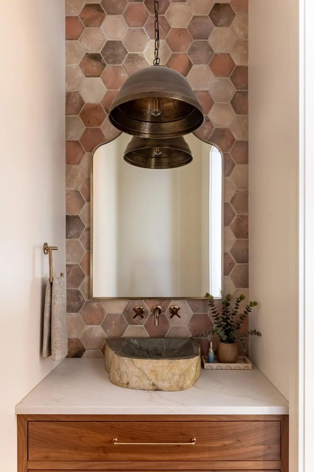 Antique brass tiered pendant above a stone vessel sink and terracotta hex tile