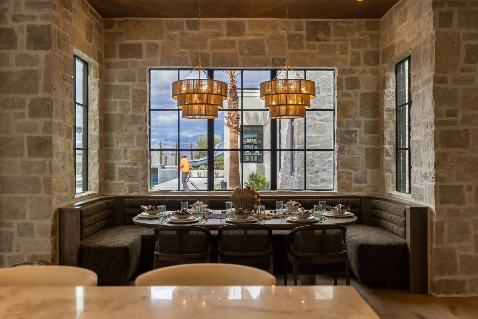 Pair of tiered woven chandeliers above a stone breakfast nook banquette