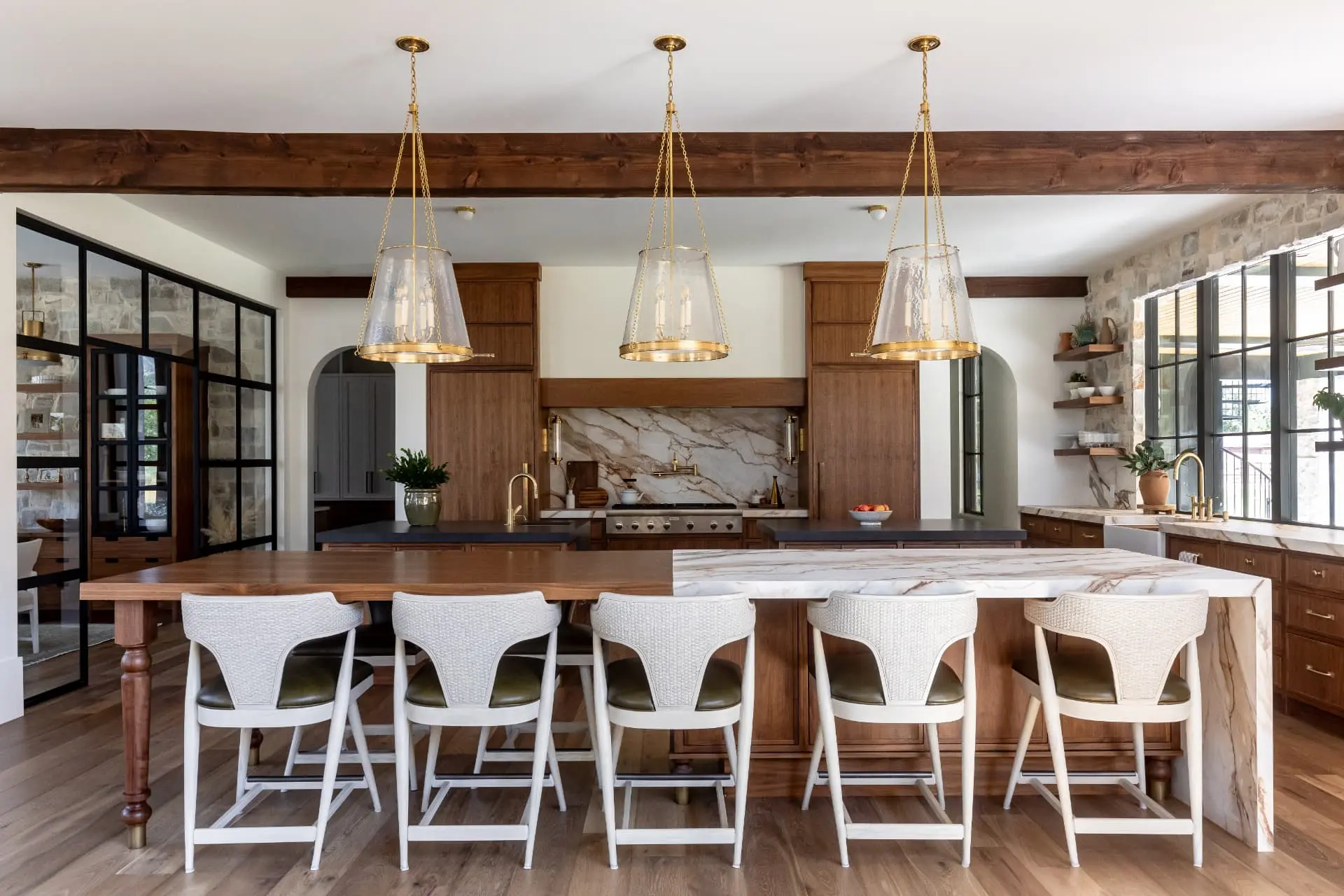 Kitchen with three chain-hung brass and seeded glass pendants above a marble and walnut island