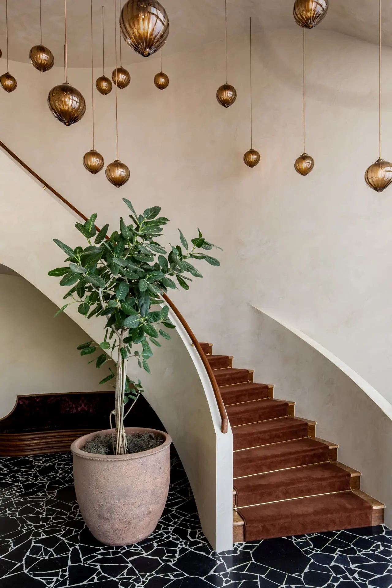 Cascading amber glass pendants above a curved plaster stair with a brown runner