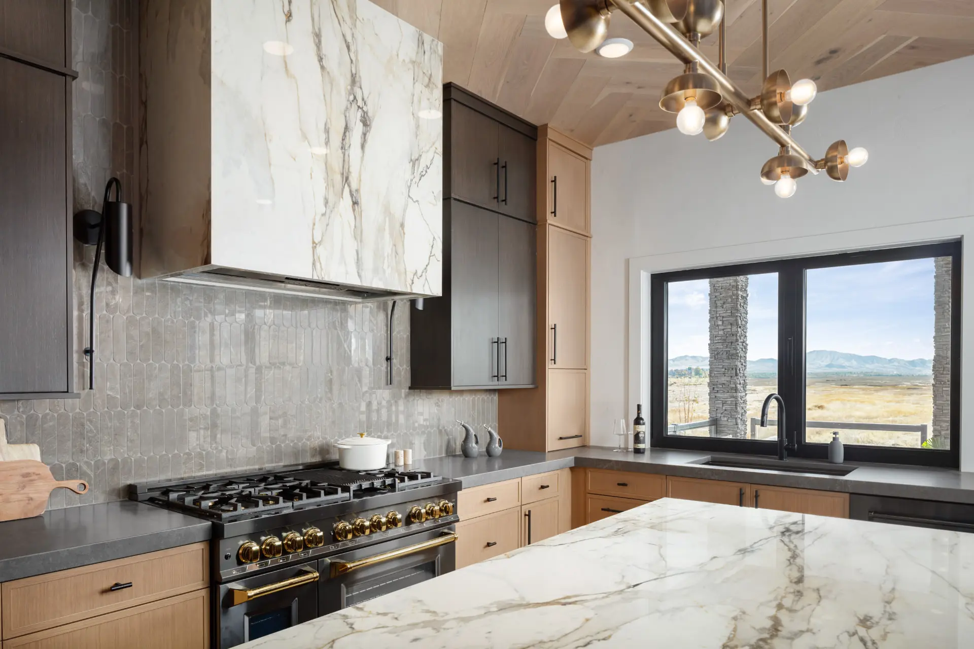 Range wall with grey picket tile, marble hood and a brass sputnik chandelier over the island