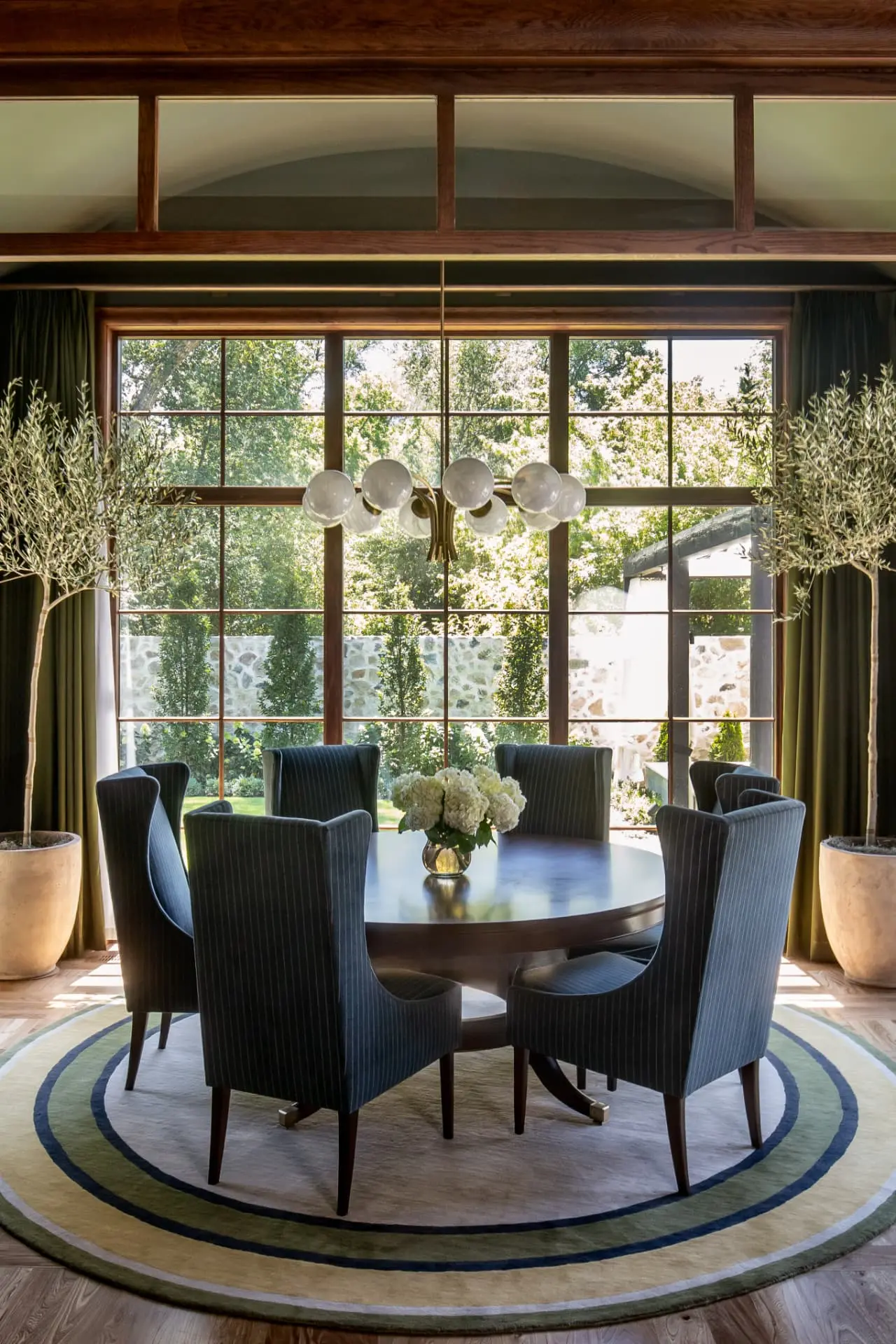 Brass and glass globe chandelier over a round dining table framed by garden windows