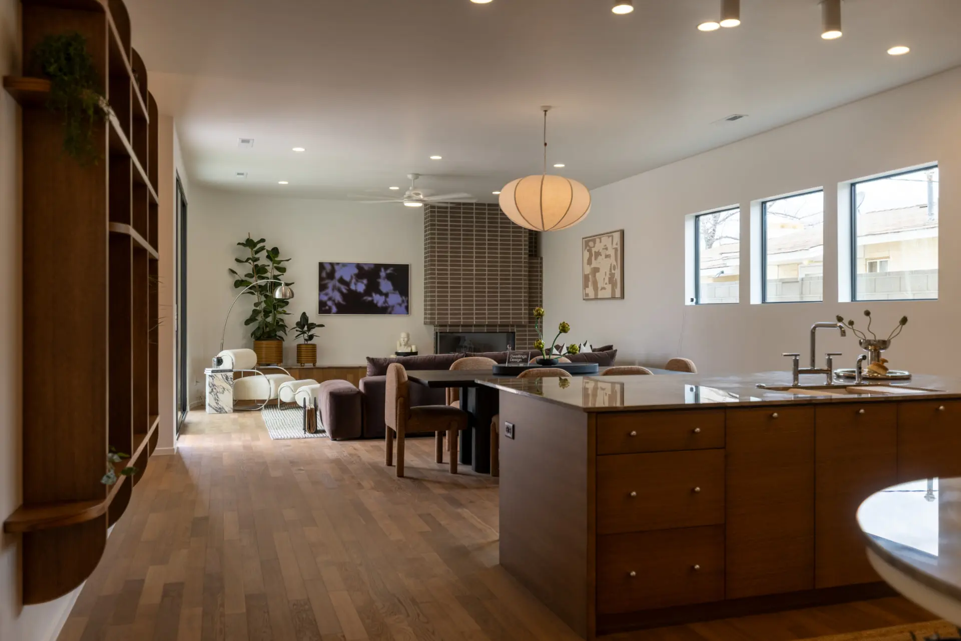 Kitchen island and open living space lit by recessed downlights and a linen pendant