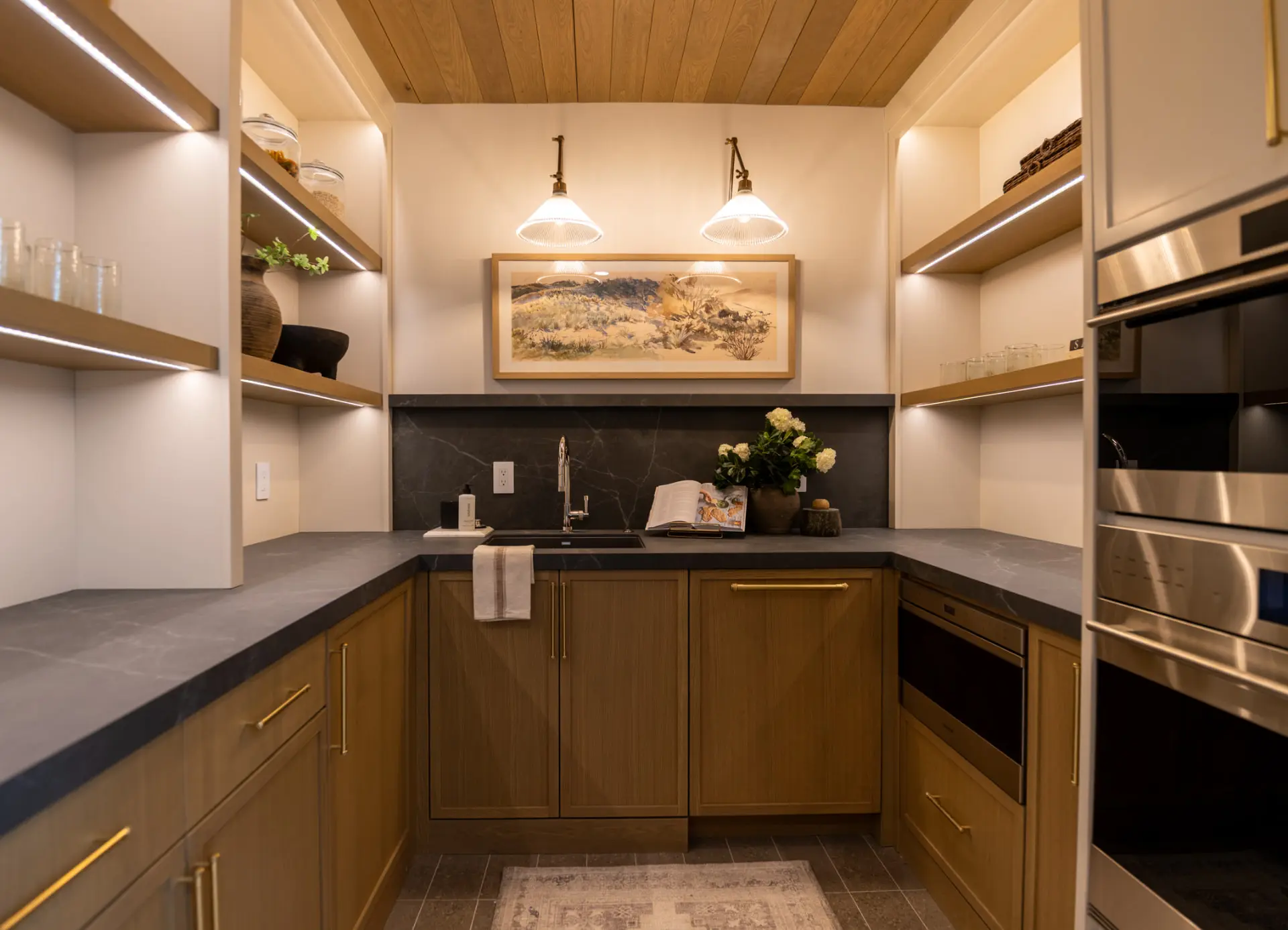 Butler's pantry with brass swing-arm sconces and lit open shelving