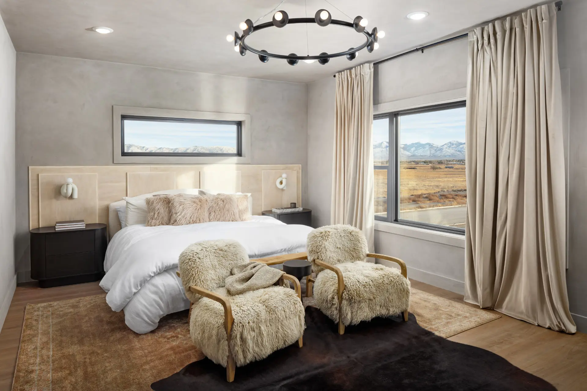 Primary bedroom in warm plaster with a blackened orbital ring chandelier and sculptural bedside sconces