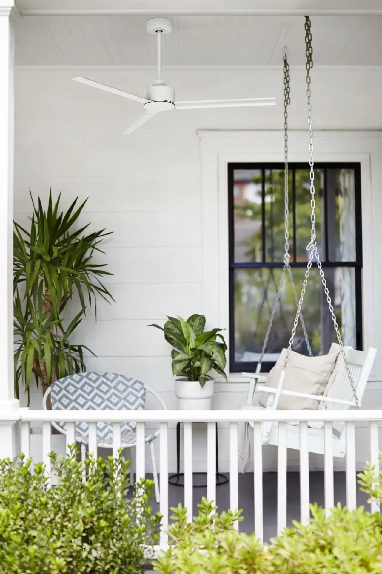 White three-blade ceiling fan above a white porch with a hanging swing and potted plants