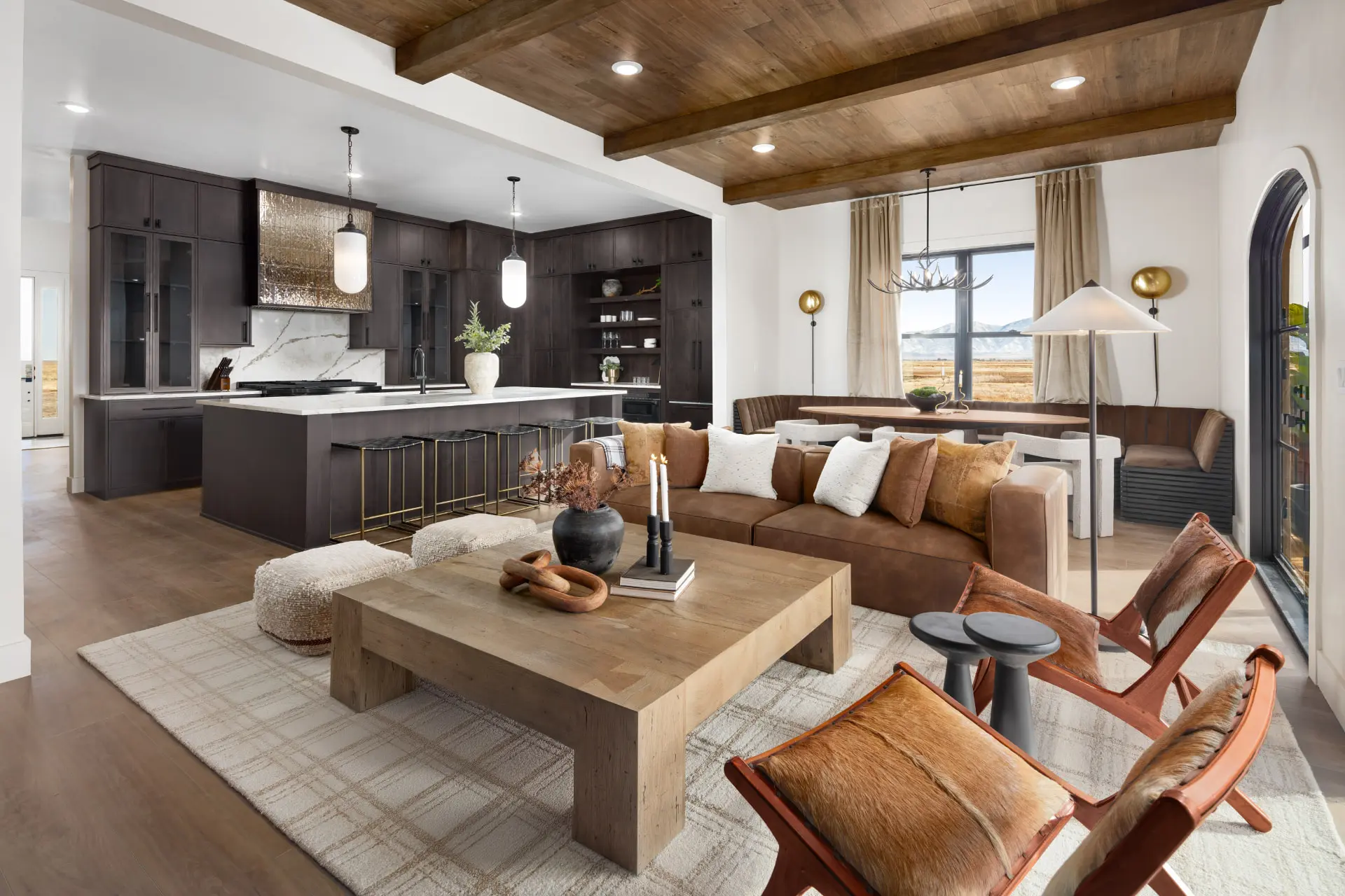 Open great room with a wood-beamed ceiling looking toward a dark walnut kitchen and dining banquette