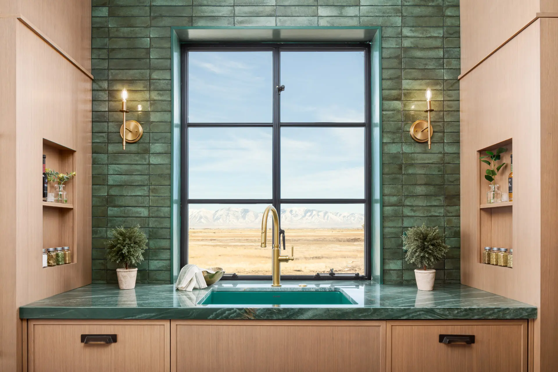Scullery sink with brass candlestick sconces on green tile and mountain views