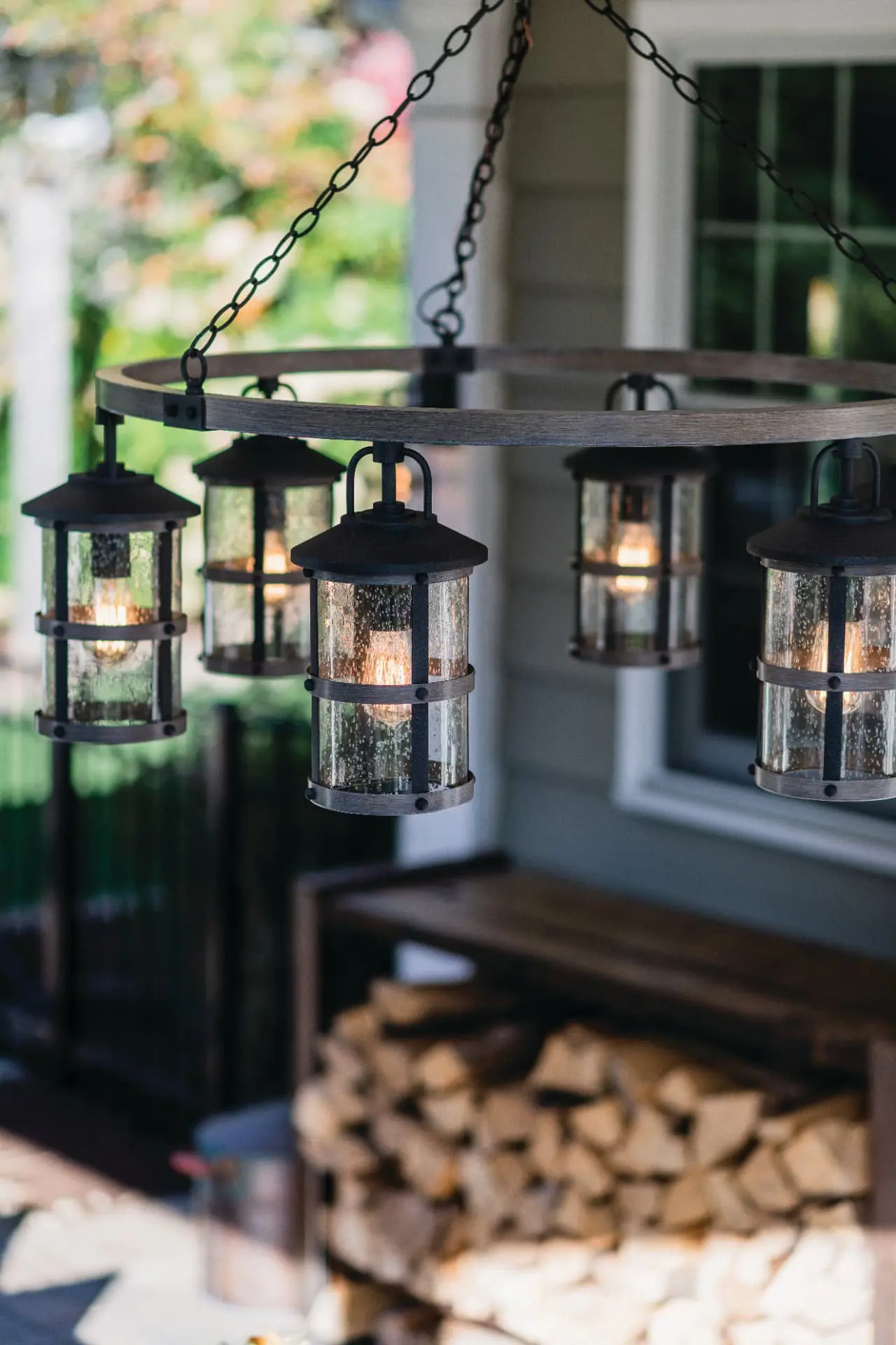 Round wood-and-iron outdoor chandelier with seeded glass lanterns glowing on a covered porch