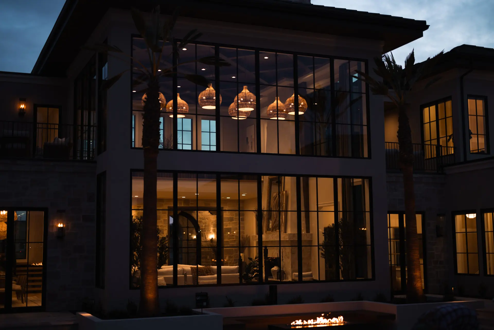 Home exterior at dusk with woven pendants glowing through two-story glass